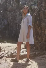 Vestido camisero corto color gris, con cuello clásico, cierre frontal de botones y mangas tres cuartos con volados en los puños.