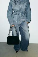 Bolso de hombro confeccionado en piel de gamuza color marrón, con diseño estructurado y pespuntes decorativos en la solapa. Cuenta con una correa de cadena metálica dorada con refuerzo de piel y cierre imantado.