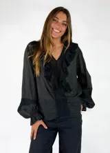 Blusa de algodón blanca con escote en V, mangas largas amplias y detalles de volados con encaje bordado en el frente.