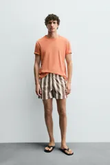 Bañador de hombre con estampado de rayas verticales anchas en tonos marrón oscuro y beige claro, con finas líneas rosadas entre ellas. Posee cintura elástica con cordón ajustable y forro interior.