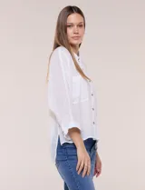 Camisa blanca de silueta holgada y textura liviana, con cuello camisero clásico, abotonadura frontal con botones en contraste y doble bolsillo de parche en el frente. Cuenta con mangas de corte dolman de largo tres cuartos con puño amplio y ruedo recto con aberturas laterales.