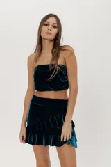 Conjunto de dos piezas de terciopelo verde oscuro, compuesto por un top strapless abuchonado y una minifalda con volados evasé.