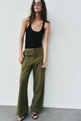 Pantalón cargo de tiro medio, color verde militar, con corte recto y bolsillos laterales de plastrón con solapa. Presenta detalles de nervios frontales y cierre con cremallera y gancho metálico.