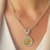 Conjunto compuesto por una cadena de eslabones redondos en plata y un dije circular con diseño de grecas en el borde y figura central en oro.