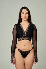 Conjunto de lencería negro de encaje y tul, compuesto por un bralette de manga larga con escote en V y una bombacha tipo tanga con detalles de encaje.