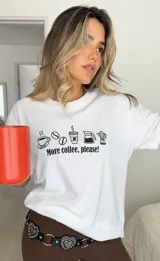 Remera blanca de algodón con estampa frontal en color negro que incluye iconos de café y la frase 'More coffee, please!'. Presenta cuello redondo y mangas cortas.