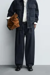 Pantalón de corte barrel fit confeccionado en denim de algodón rígido color azul oscuro. Presenta cintura con pliegues frontales, bolsillos laterales y bolsillos traseros de vivo. Cierre frontal con cremallera y gancho metálico oculto.