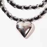 Gargantilla de doble cadena, una de eslabones plateados y otra de cordón trenzado negro, con dije de corazón plateado.