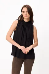 Blusa sin mangas de color negro, con cuello alto y diseño plisado en el frente que le otorga una caída fluida y holgada.