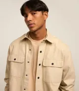 Camisa de manga larga confeccionada en sarga de algodón color verde menta, con cuello inglés y cierre frontal de botones negros. Presenta dos bolsillos de parche con solapa en el pecho y puños con botones.