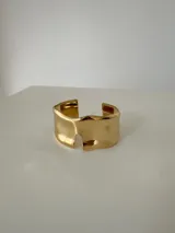 Brazalete rígido de diseño abierto con acabado pulido y forma orgánica irregular, fabricado en acero quirúrgico.