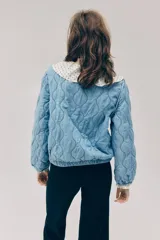 Campera acolchada ligera de denim en mezcla de algodón y lyocell, modelo Divided de H&M. Presenta cuello redondo, cierre frontal con botones a presión, hombros ligeramente caídos, mangas abullonadas y elástico revestido en los puños y el dobladillo inferior. Diseño pespunteado con ondas.