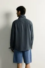 Camisa relaxed fit de lino color negro con efecto lavado, cuello clásico, manga larga con puños abotonados y dos bolsillos de parche con solapa en el pecho.