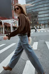 Camisa marrón de manga larga con cuello solapa y cierre frontal de botones. Los puños terminan con lazos anudados.