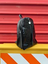 Mochila negra con textura símil cuero de cocodrilo, con bolsillo vertical delantero con cierre y bolsillo oculto en la espalda.