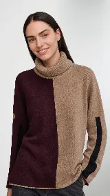 Polera de cuello alto confeccionada en lana lambswool, con diseño bicolor en negro y marrón. Presenta mangas largas con franjas verticales en gris y un parche circular bordado en la manga derecha.