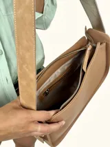 Bolso tipo baguette de cuero genuino color marrón claro, con dos compartimentos frontales con solapa y un parche de gamuza con el logo de un búho grabado. Posee una correa ancha de cuero ajustable.