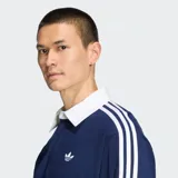 Polo de rugby Adidas de manga larga, color azul marino con cuello y botones blancos. Presenta las icónicas tres tiras blancas en los hombros y mangas, y el logo del trifolio bordado en el pecho.