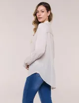 Camisa Magaschoni de silueta holgada y tejido texturizado color blanco, con cuello camisero, cierre frontal de botones, mangas largas con presilla para arremangar y diseño asimétrico con espalda más larga.