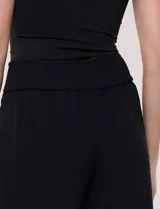 Pantalón negro de calce relajado y caída fluida, confeccionado en poliéster con textura de crepé. Tiene cintura alta elastizada estilo pull on con un aplique de cadena metálica decorativa, y pierna de corte ancho tipo wide leg corto por arriba del tobillo.