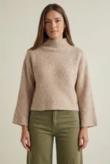 Polera de lana color beige con diseño de tejido acanalado, cuello alto y mangas largas con corte ligeramente acampanado. Presenta un calce holgado y cómodo.