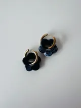 Aros de acero quirúrgico hipoalergénico con argolla dorada y dije colgante en forma de flor de resina marmolada en tonos negros y grises.