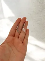 Aritos tipo argolla pequeña con dije colgante en forma de ala calada, fabricados en acero quirúrgico.