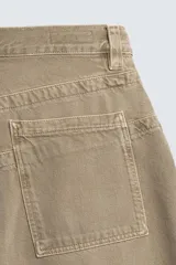 Jeans de hombre, tiro medio, color marrón claro o caqui, con corte relaxed fit y perneras anchas. Presenta cinco bolsillos y costuras laterales giradas hacia el frente.