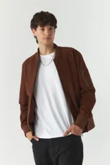 Campera bomber negra de simil gamuza, con cuello redondo, cierre frontal con cremallera, bolsillos laterales con cierre y puños elásticos.