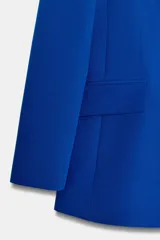 Blazer entallada de color azul vibrante, con cuello de solapa de muesca, manga larga con hombreras y cierre frontal de dos botones forrados. Presenta bolsillos delanteros con solapa y forro interior en color negro.