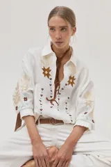 Camisa blanca de lino con bordados florales en tonos dorados y marrones en el frente y las mangas.