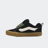 Championes Vans modelo Knu Skool, de color negro con la clásica franja lateral Sidestripe blanca. Presentan diseño robusto de estilo noventero, lengüeta y cuello acolchados, cordones anchos en color verde militar y suela de goma marrón.