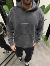 Canguro con capucha de algodón en color gris oscuro con efecto lavado, corte holgado, bolsillo tipo canguro frontal y logo pequeño estampado en el pecho.