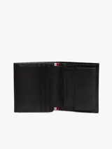 Billetera plegable en tres partes de cuero negro con textura acanalada. Presenta un logo esmaltado de la marca en la esquina inferior derecha. Incluye compartimentos para billetes, ranuras para tarjetas y un bolsillo para monedas.