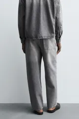 Pantalón de jeans de algodón, color gris oscuro con efecto lavado. De tiro medio y corte relajado con pierna recta desde la cadera hasta el tobillo. Presenta cinco bolsillos y cierre frontal con botonadura.