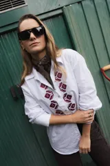 Camisa de algodón color marrón con corte clásico y cuello camisero. Presenta un bordado geométrico en color negro en la parte frontal y mangas largas con puños abotonados.