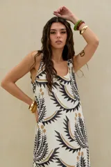 Vestido largo de color blanco con estampado gráfico en tonos negros y dorados, sin mangas y con escote redondo.