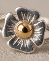 Anillo de plata con diseño de flor y detalle central dorado.
