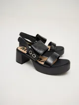 Sandalias de cuero color marrón con plataforma y taco cuadrado. Presentan dos tiras anchas sobre el empeine y una tira trasera con elástico. Decoración de doble argolla en los laterales.