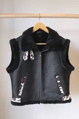 Chaleco de cuero negro con interior de piel sintética negra. Presenta detalles en piel con estampado de vaca en los bolsillos, el ruedo y la zona del cuello. Cierre frontal con cremallera.