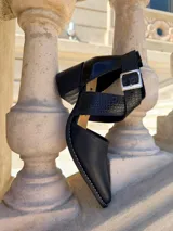 Zapatos de cuero color tostado con puntera fina y taco bloque de madera de 6 cm. Cuentan con tiras cruzadas con estampado animal print de leopardo en el empeine, talón negro y tira al tobillo con hebilla metálica ajustable.