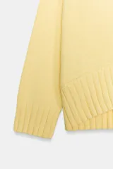 Sweater de punto color amarillo claro, con cuello redondo, manga larga y dobladillo asimétrico más largo en la parte trasera. Presenta acabados en rib en cuello, puños y ruedo.