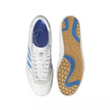 Championes adidas modelo Puig Indoor, de diseño bajo en color blanco con las icónicas tres tiras en azul claro y detalles en gamuza gris en el talón y la zona de los cordones. Presenta el nombre del modelo en dorado en el lateral.