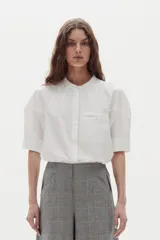 Camisa de algodón color blanco, con cuello mao, botonadura oculta y mangas cortas raglán con cortes estructurados.