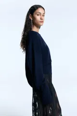 Sweater de tejido de punto color azul marino, con diseño de silueta holgada, cuello redondo y mangas largas con puños acanalados anchos que incluyen orificio para el pulgar. Presenta un detalle de aplicación de hotfix brillante en el frente y un ruedo acanalado ancho.