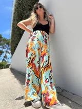 Pantalón palazzo de tiro alto con estampado abstracto en tonos naranja, rojo y negro sobre fondo celeste.
