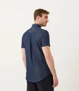 Camisa azul de manga corta con cuello clásico, corte slim fit, cierre frontal con botones blancos y bolsillo de parche en el pecho.