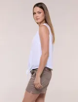 Blusa blanca sin mangas, confeccionada en algodón con sutiles rayas verticales en relieve. Presenta cuello redondo, cierre frontal con botones de madera y un nudo ajustable en el dobladillo delantero.