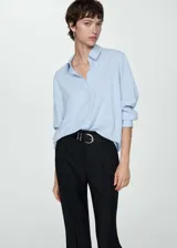 Camisa de corte recto y tejido fluido, color celeste, con cuello camisero, cierre frontal de botones y mangas largas con puños abotonados.
