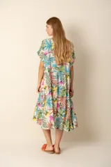 Vestido largo estampado con flores en tonos violeta, naranja, verde y azul sobre un fondo beige claro. Tiene cuello en V y mangas cortas.